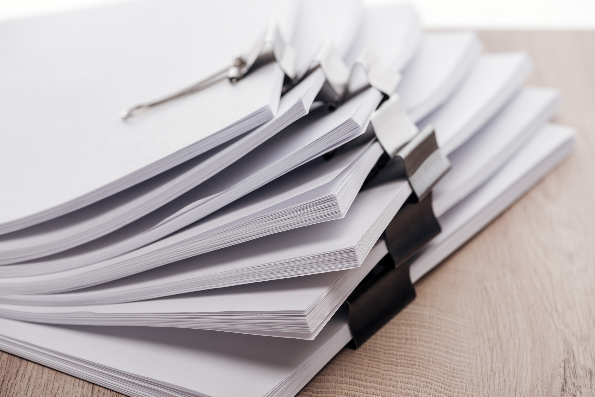 A stack of white papers sitting on top of a wooden table.