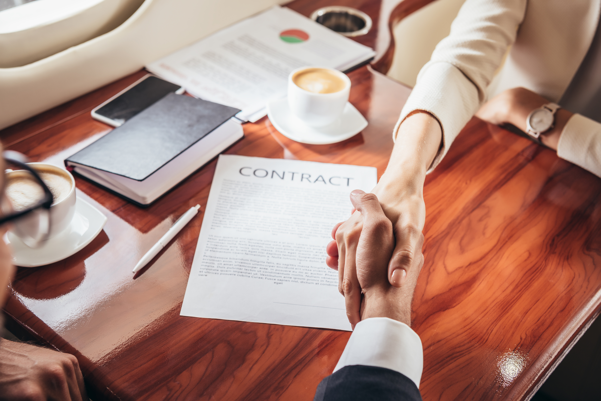 Two people shaking hands over a signed document.
