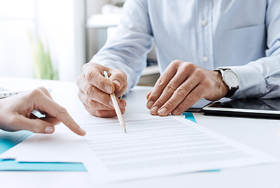 Two people sitting at a table with papers and a pen.